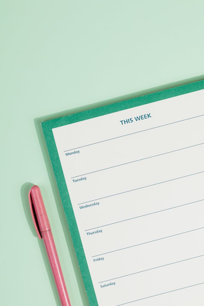 Minimalistic image of a weekly planner with a pink pen on a pastel green background.